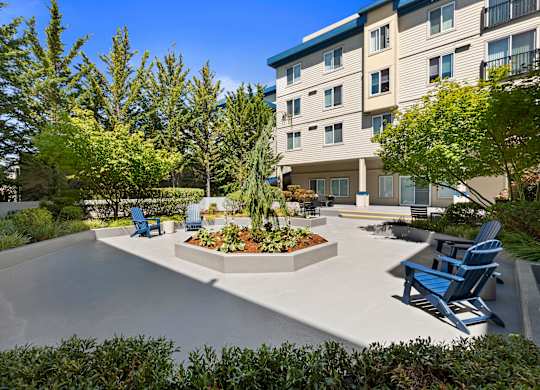 a courtyard with a large tree in the center and a seating areas with blue Adirondack chairs at Guinevere Apartment Homes, Seattle