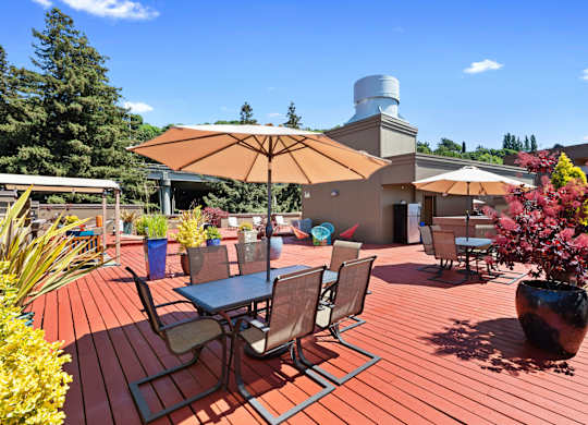 a large wooden deck with tables and chairs for lounging and potted flowers at Illumina Apartment Homes, Washington, 98102