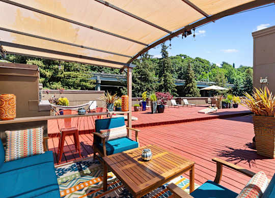 Shaded Wooden Deck Area with blue chairs and a wooden table for Relaxing at Illumina Apartment Homes, WA 98102