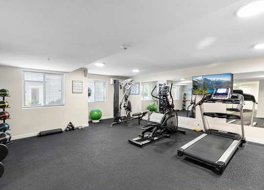 a gym with exercise equipment and a flat screen tv at West Mall Place Apartment Homes, Everett, WA