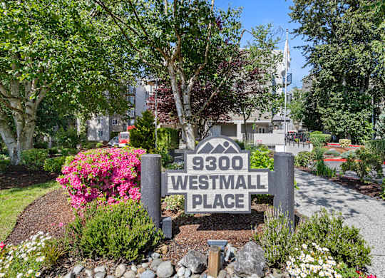 Property Sign with Address surrounded by flowers and trees in the background at West Mall Place Apartment Homes, Everett, Washington