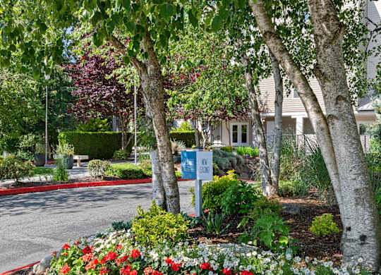 Entrance with trees and flowers in front of property building at West Mall Place Apartment Homes, Everett, WA