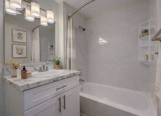 A white bathroom with a marble countertop and a white bathtub.