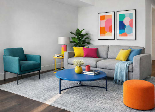 A living room with a grey couch, a blue coffee table, a green chair, a yellow side table, and a potted plant.