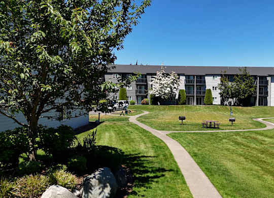 A grassy area with benches and a walking path in front of apartment buildings.