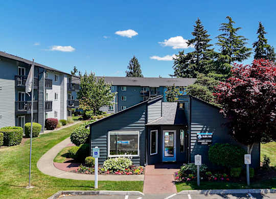 A small building with a blue door is surrounded by greenery and other buildings.