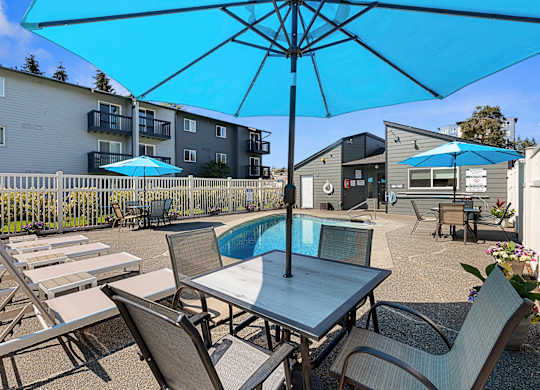 a patio with a pool and chairs and umbrellas at Pacific Park Apartment Homes, WA 98026