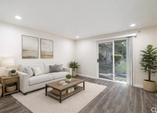 A living room with a grey couch, a wooden coffee table, and a large window with a view of the backyard.