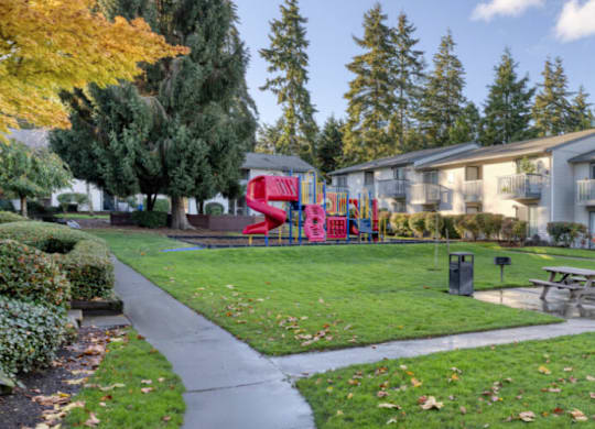 a yard with a picnic table and a red slide in front of houses at Pinewood Square Apartment Homes, Lynnwood, WA, 98036