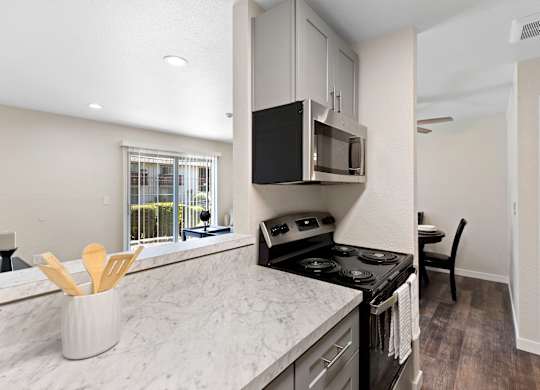 Cozhy Kitchen with Stainless Steel Appliances, Plank Flooring, Spacious Cabinetry, and View of the Living Area at Pinewood Square Apartment Homes, Lynnwood, WA