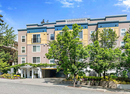 an apartment building with yellow and blue siding and a tree in front of it at Sir Gallahad Apartment Homes, Washington