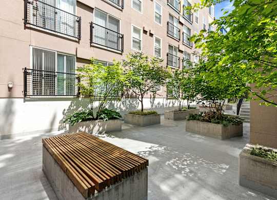 a courtyard with a wooden bench and trees in front of  Sir Gallahad Apartment Homes, Washington, 98004