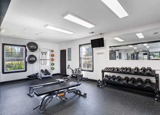 A gym with a row of dumbbells on the right and a bench on the left. at Village on the Lake Apartments, North Carolina, 28390