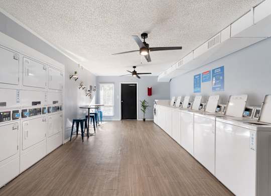 A laundry room with a washer and dryer on the wall and a table with two chairs at Lakes Edge Apartments, Greensboro, NC, 27409
