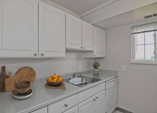 A kitchen with white cabinets and a countertop with a bowl of fruit on it.