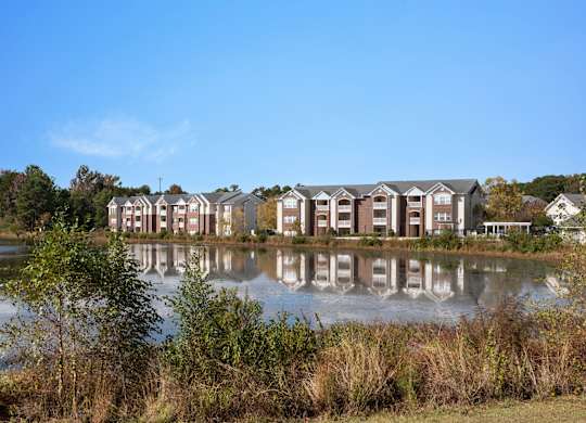 A row of houses are reflected in the water. at Village on the Lake Apartments, Spring Lake, 28390