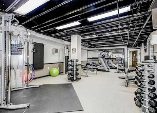 A gym with a variety of equipment including weights and a bench. at Park Georgetown Apartments, Arlington, Virginia