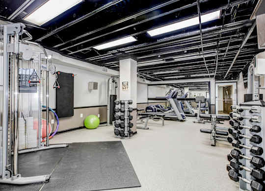 A gym with a variety of equipment including weights and a bench. at Park Georgetown Apartments, Virginia, 22209