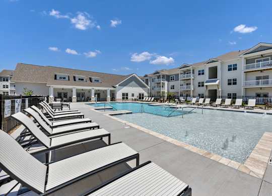 A pool area with sun loungers and apartment buildings in the background.