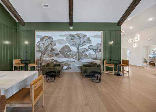 A room with a large mural of a tree on the wall and several chairs and tables scattered around.