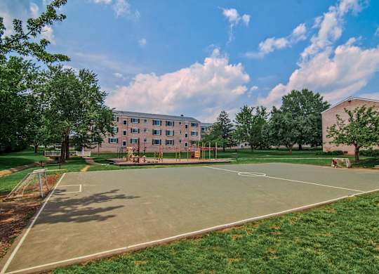 A basketball court is surrounded by grass and trees in front of a building at Dulles Glen Apartments, Herndon, Virginia
