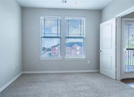 A room with a carpeted floor and a view of a house through the window.