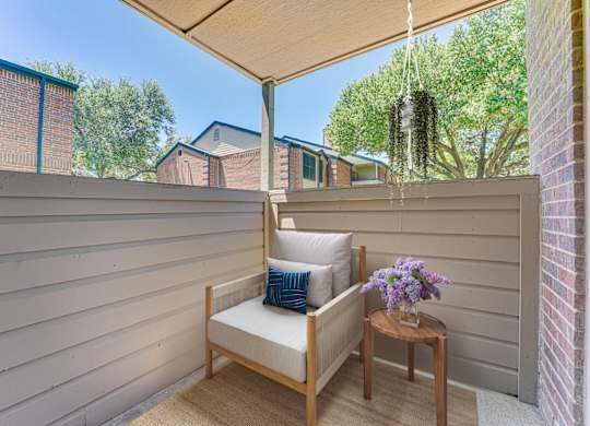 A wooden chair with a cushion and a small table with flowers on it. at Indian Creek Apartments, Carrollton, TX, 75007