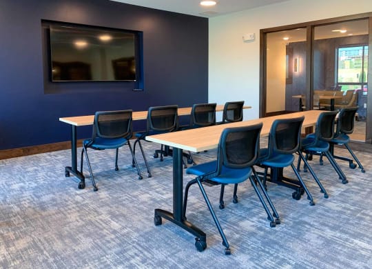 A conference room with large tables and chairs facing a presenting TV
