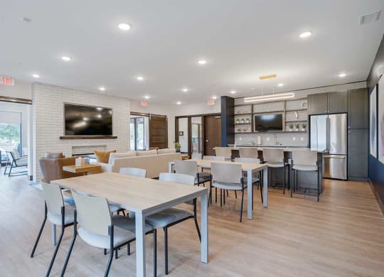 a community room with a kitchen, tables and chairs, and seating in front of a tv and fireplace