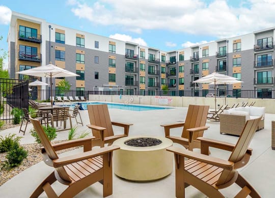 a firepit in front of a pool with chairs and umbrellas in front of an apartment building