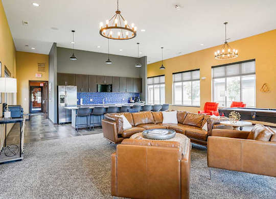 A clubhouse kitchen with large island and several bar stools, and a lounge area with a leather couch, chairs, and a pool table.