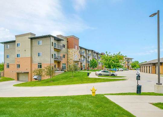 The side of a brick apartment building with green lawns, and a drive leading to an underground parking garage.