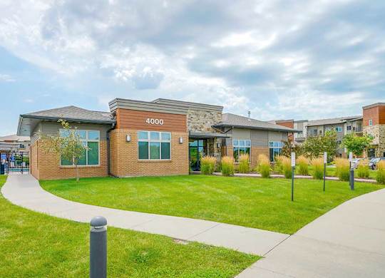 A modern clubhouse with a professionally landscaped green lawn.