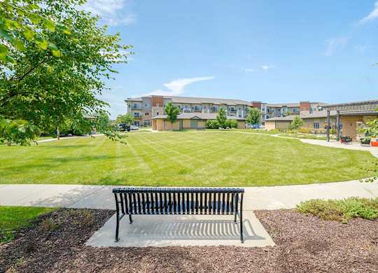 An expansive green courtyard lawn with a walking path around the edge, and a bench to rest on.