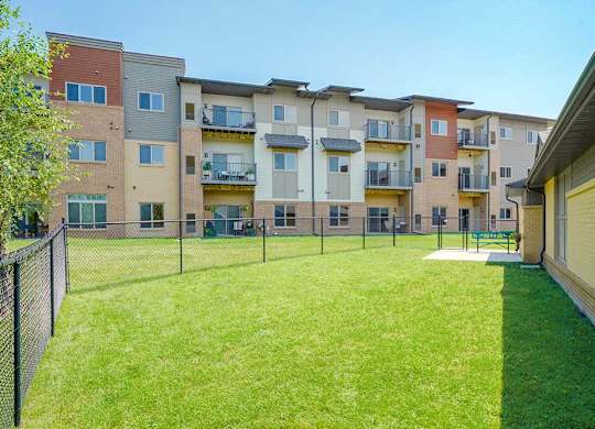 A fenced-in grassy dog park with a bench and plenty of room for your dog to run around off leash.