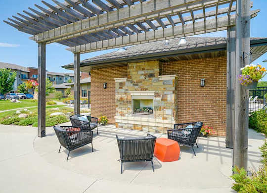 A patio with a stone fireplace and chairs under a pergola.