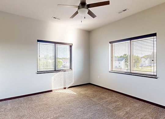 A bedroom with a ceiling fan, and two windows - one on each wall.