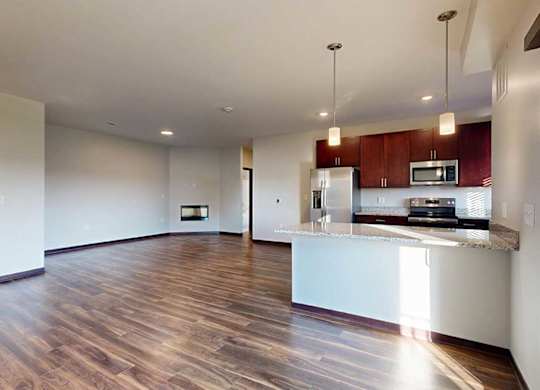 A living room with wooden flooring, next to an open kitchen with dark wooden cabinets and a peninsula counter.