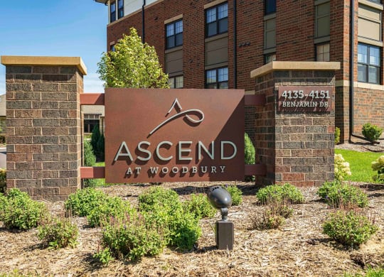 outdoor brick sign for Ascend at Woodbury in front of apartment building