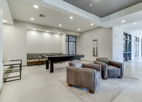 Game room in Ascend at Woodbury apartments' clubhouse with pool table and leather chairs.