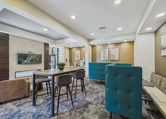 Modern apartment community lounge with teal seating, a high-top table, wall-mounted TV, and recessed lighting