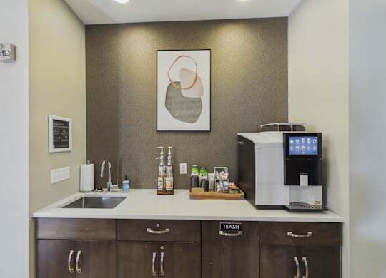 Apartment community coffee station with dark wood cabinetry, sink, beverage supplies, and a countertop coffee machine.