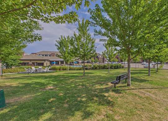 Landscaped apartment community courtyard with mature trees, grassy lawn, walking paths, and outdoor benches.