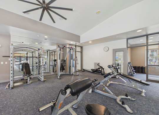 Apartment community fitness center with weight-training machines, cardio equipment, rubber flooring, and a large ceiling fan.