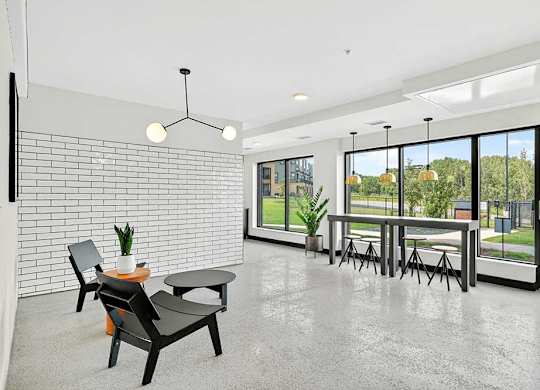 Bright apartment community lounge with polished concrete floors, modern seating, white tile accent wall, and large windows with views of green outdoor space.