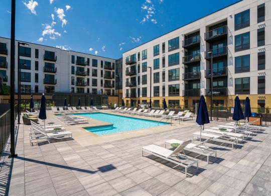 Resort style swimming pool with white sun loungers and green circular side tables at Aspire at CityPlace