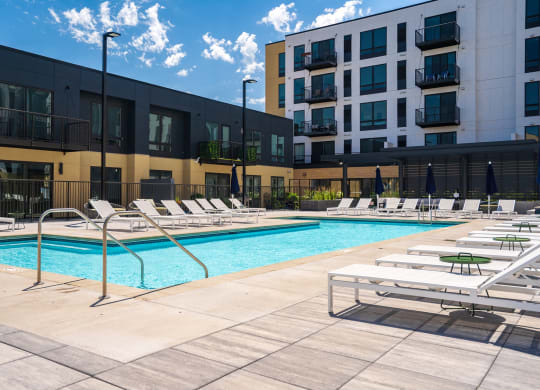 Resort style swimming pool with white sun loungers and green circular side tables at Aspire at CityPlace