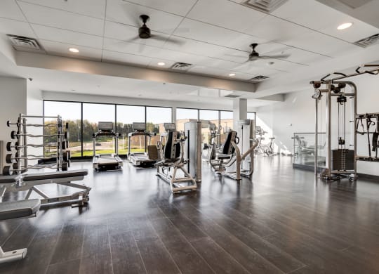 Fitness center with full-wall windows and dark brown wood floors in luxury apartment