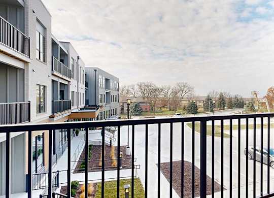 a balcony with a black railing overlooks a parking lot and apartment buildings