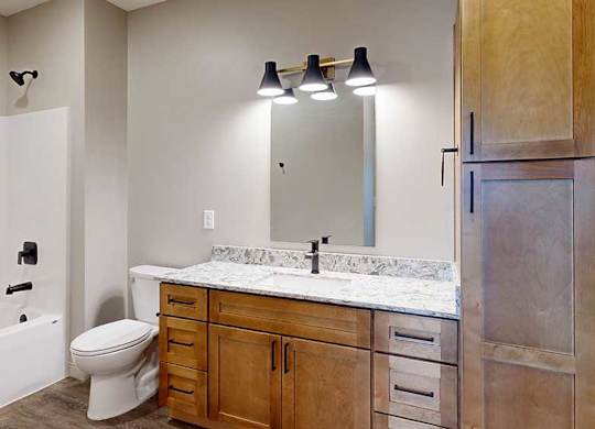a bathroom with a light brown cabinets, a tall storage cabinet, quartz vanity sink, a mirror, and a shower and tub